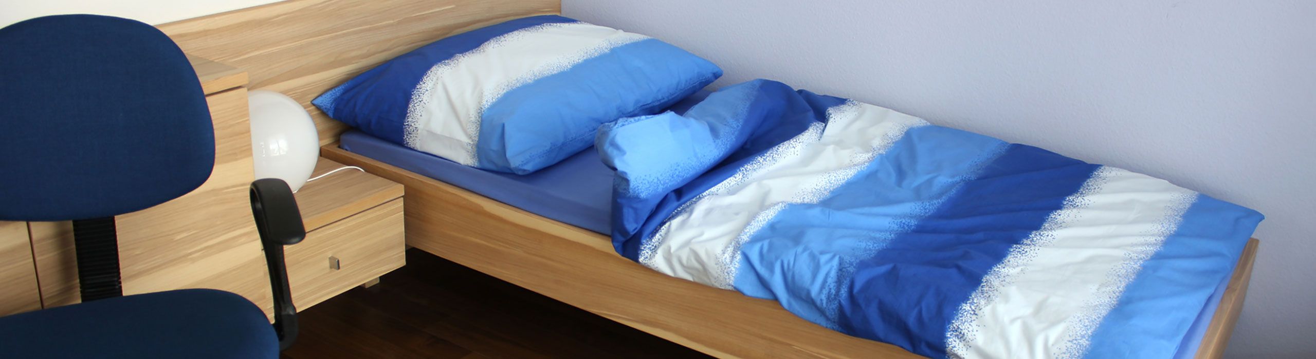 Schlafzimmer der Trainingswohnung mit blau-weißer Bettwäsche